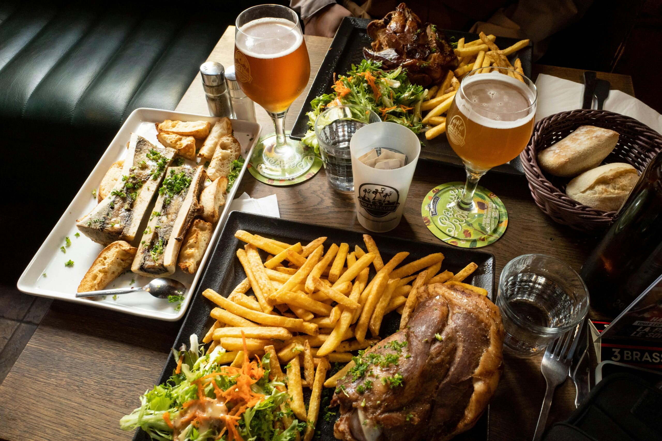 A hearty French meal with bone marrow, fries, salad, and beer served on a rustic wooden table.