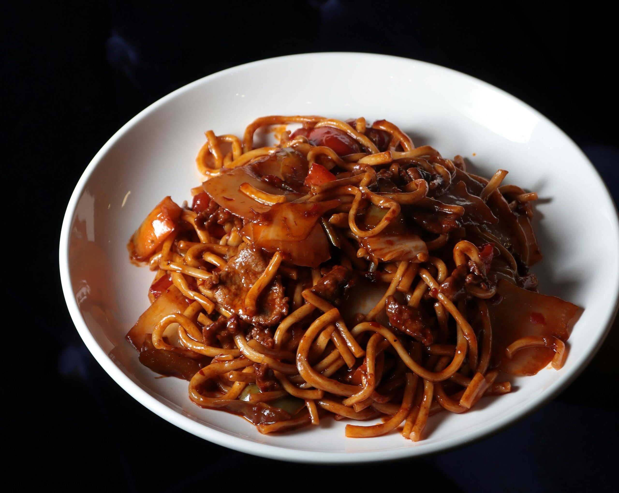 Close-up of flavorful stir-fried noodles with beef, vegetables, and savory sauce on a white plate.